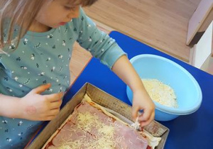 Dzieci sypia serem prawie gotową pizzę.